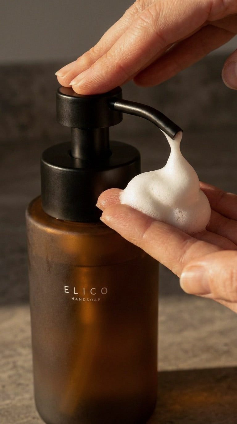 Närbild på en hand som pumpar mjukt skum ur en dispenser av bärnstensglas