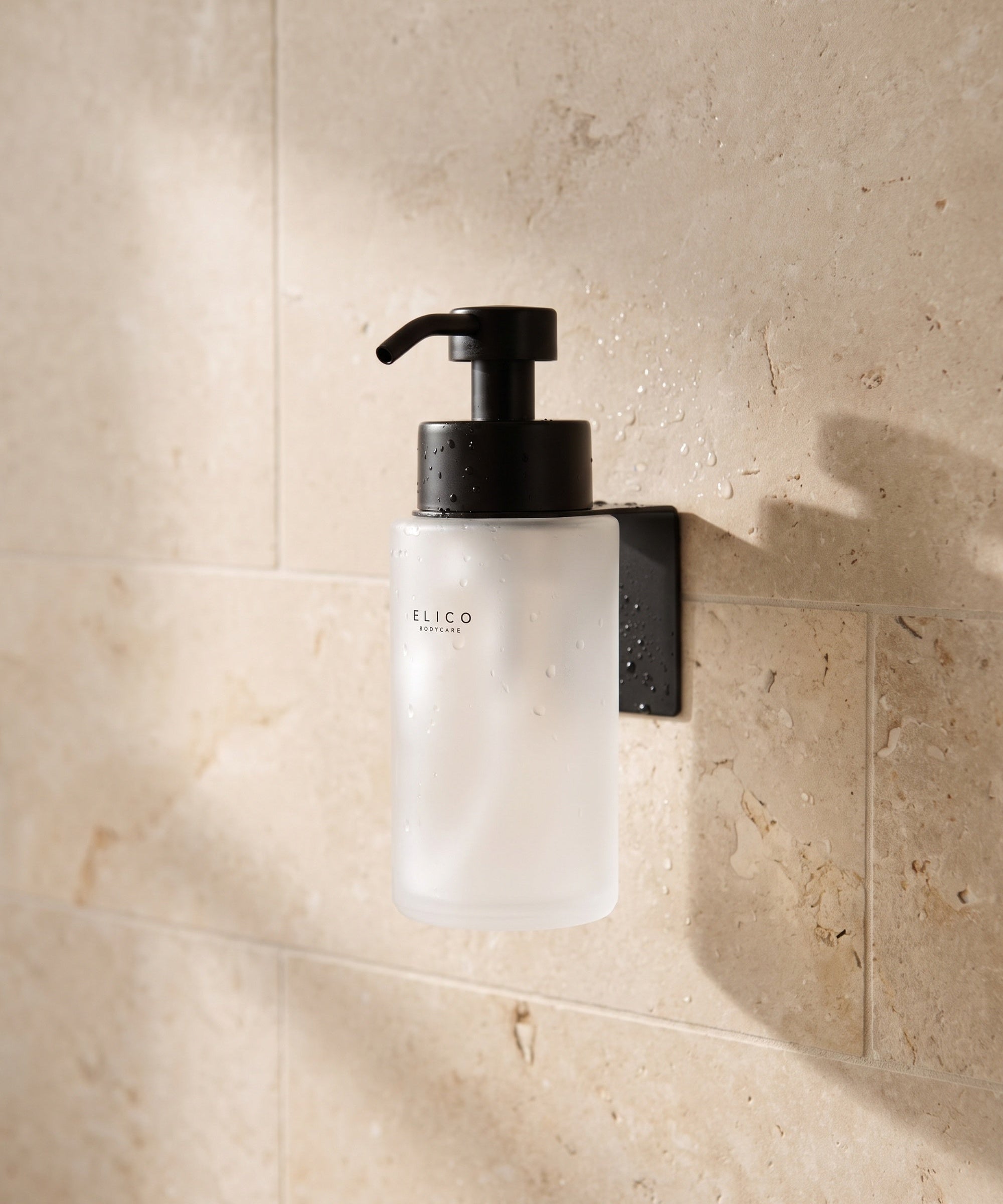 Frostad Elico Bodycare-dispenser i det matt svarta väggfästet på en kalkstensvägg i duschen